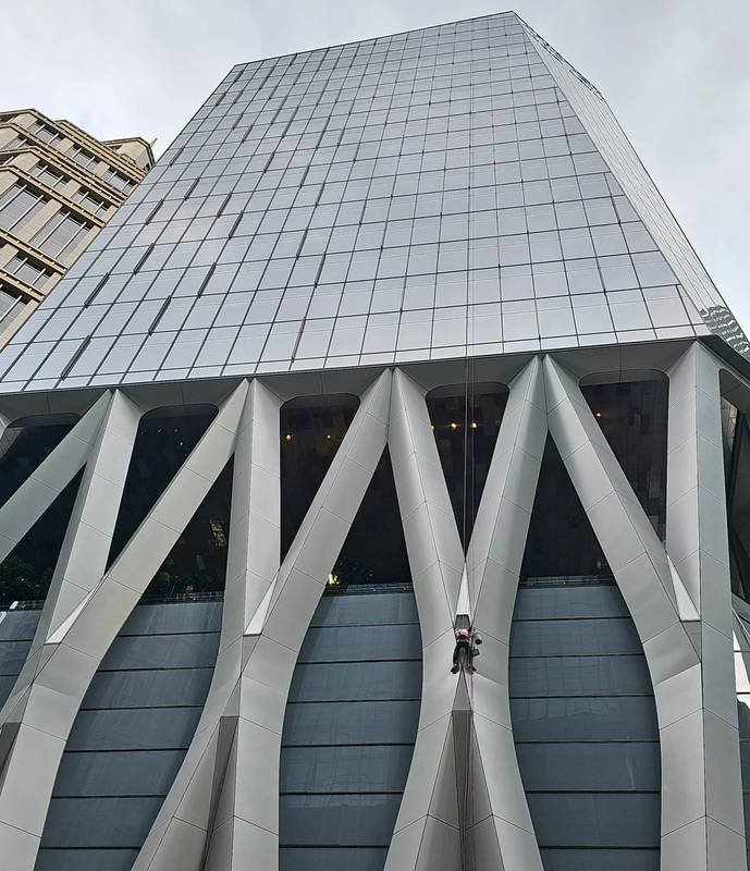 rope access technician on a sculpted glass façade carrying out lighting works in Singapore